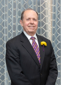 A man wearing a purple and gold striped tie smiling.