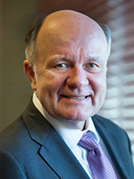 A headshot photo of a man wearing a suit and purple tie