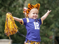 A small girl wearing an LSU football jersey and plush tiger ears plays with a pom pom