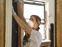 A student wearing a breathing mask tears down drywall