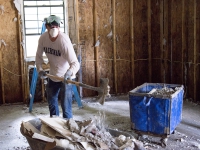 A man wearing a breathing mask scoops drywall from a floor