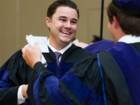A male student wears a graduation robe and smiles
