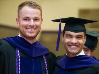 Two male students wearing graduation attire smile for a photo