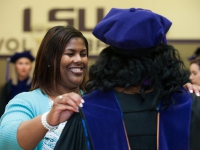 A woman adjusts a female student's graduation attire