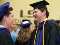 Two male students wearing graduation attire smile