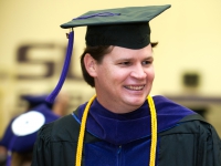 A male student wears a graduation robe and cap and smiles