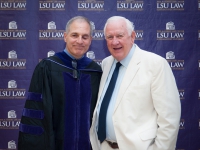 Two men smile for a photo with the LSU Law logo in the background
