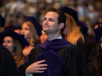 A male student wearing graduation attire places his hand over his heart