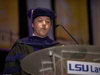 A male student wearing graduation attire speaks at a podium