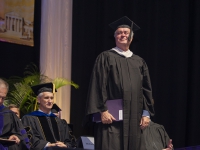 A man wearing graduation attire stands