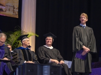 A man wearing graduation attire stands