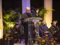 A man wearing graduation attire speaks at a podium