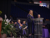 A woman wearing graduation attire speaks at a podium