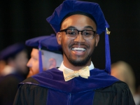 A students wearing graduation attire smiles