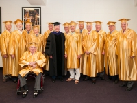 A group of men wearing gold robes poses for a photo with a man wearing a black robe