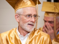 A man wearing a gold graduation cap and gown smiles