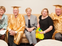 Men wearing a gold graduation cap and gown smile seated next to women