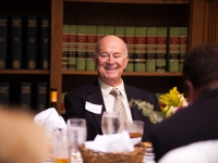A man wearing a suit and tie is seated at a table and smiles