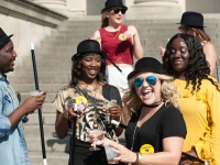 Females wearing black hats and holding canes smile