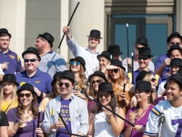 A group of students wearing black hats and holding canes lift champagne glasses in the air