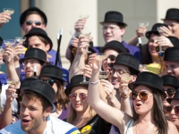 A group of students wearing black hats and holding canes lift champagne glasses in the air