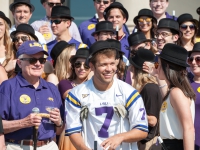 A man  wearing an LSU hat stands next to a group of students