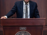 A man wearing a suit and tie speaks at a podium