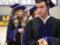 A male student wears a graduation robe and cap and looks to the left