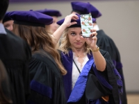 A female student wears a graduation robe and cap and looks at her phone
