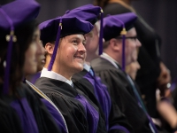 A male student wearing graduation attire smiles