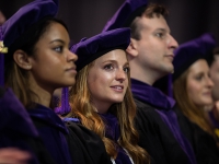 A female students wearing graduation attire looks on