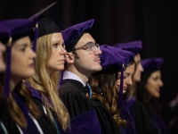 A male students wearing graduation attire looks on