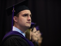 A male students wearing graduation attire looks on