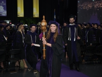 A female student wearing graduation attire carries a wooden mace