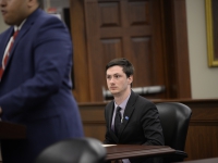 A male student wearing a suit and tie sits at a table and takes notes