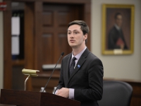 A male student wearing a suit and tie speaks at a podium