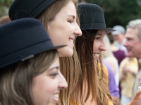 Three women wearing derby hats smile for a photo
