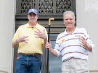 Two men smile for a photo holding a black and gold cane
