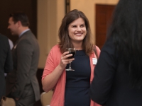 A female student holds a glass of wine and smiles as she talks to a person