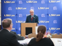 A man wearing a suit and tie speaks at a podium with the LSU Law logo in the background