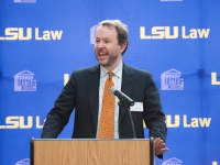 A man wearing a suit and tie speaks at a podium with the LSU Law logo in the background