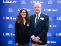 A female student and a man pose for a photo with the LSU Law logo in the background