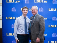 A male student and a man pose for a photo with the LSU Law logo in the background