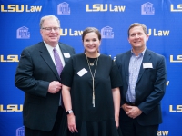 A female student and two men pose for a photo with the LSU Law logo in the background