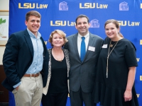 Four people pose for a photo with the LSU Law logo in the background