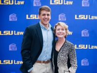 A male student and a woman pose for a photo with the LSU Law logo in the background
