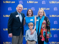 Four people pose for a photo with the LSU Law logo in the background