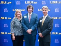 A male student and a man and a woman pose for a photo with the LSU Law logo in the background
