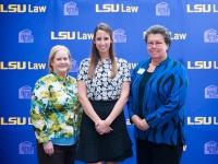 A female student and a two women pose for a photo with the LSU Law logo in the background