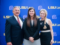 A female student and a man and a woman pose for a photo with the LSU Law logo in the background